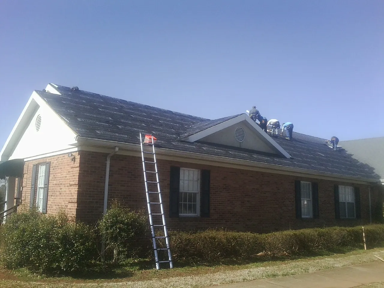 Crew tearing shingles off a brick ranch roof with a ladder set — Emergency Roof Repair work by our crew in Granada Hills