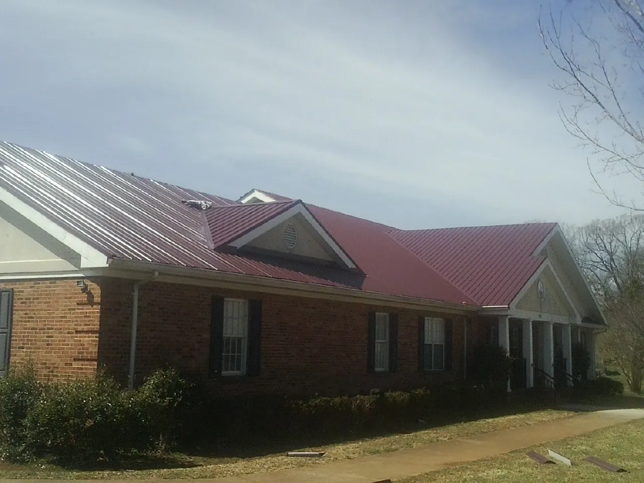 Red metal roof with gabled entries on a long brick building, from a Hail Damage Roof Repair job in Granada Hills
