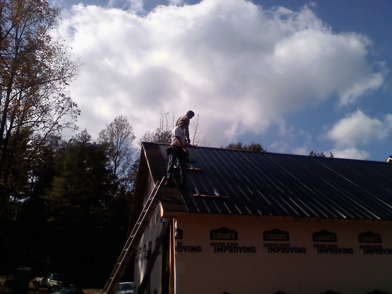Roofer fastening dark metal panels high against a cloudy sky, from a Roof Inspection job in Granada Hills