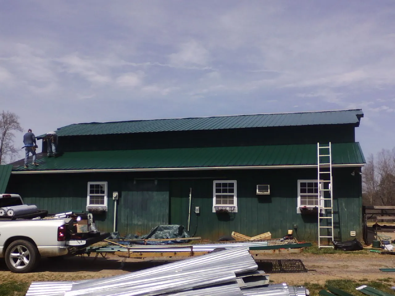 Crew installing green metal roofing on a large green barn in Granada Hills