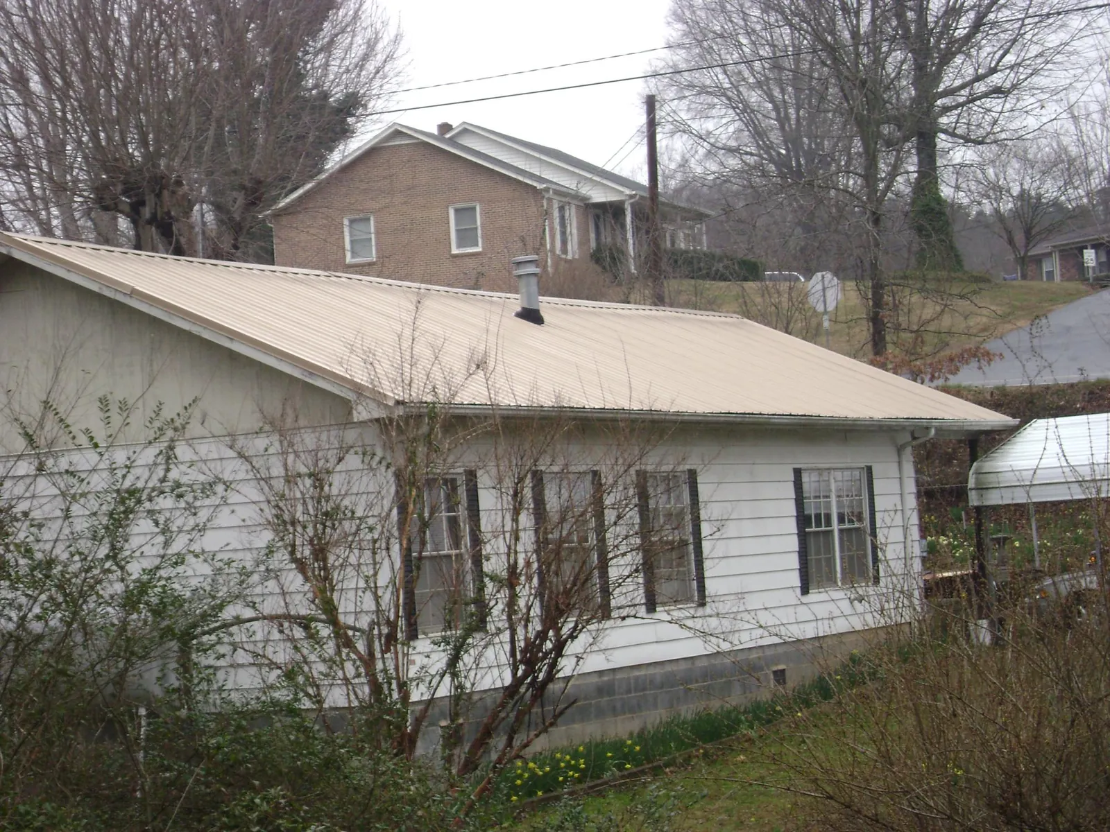 Tan metal roof on a white sided house set into a hillside — Commercial Roofing by Roofing Brothers in Granada Hills